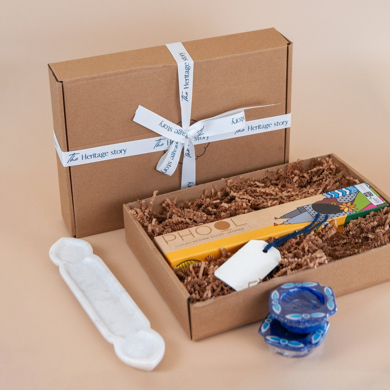 Gift box with marble incense holder, artisnalincense sticks and blue pottery tealights on a beige background
