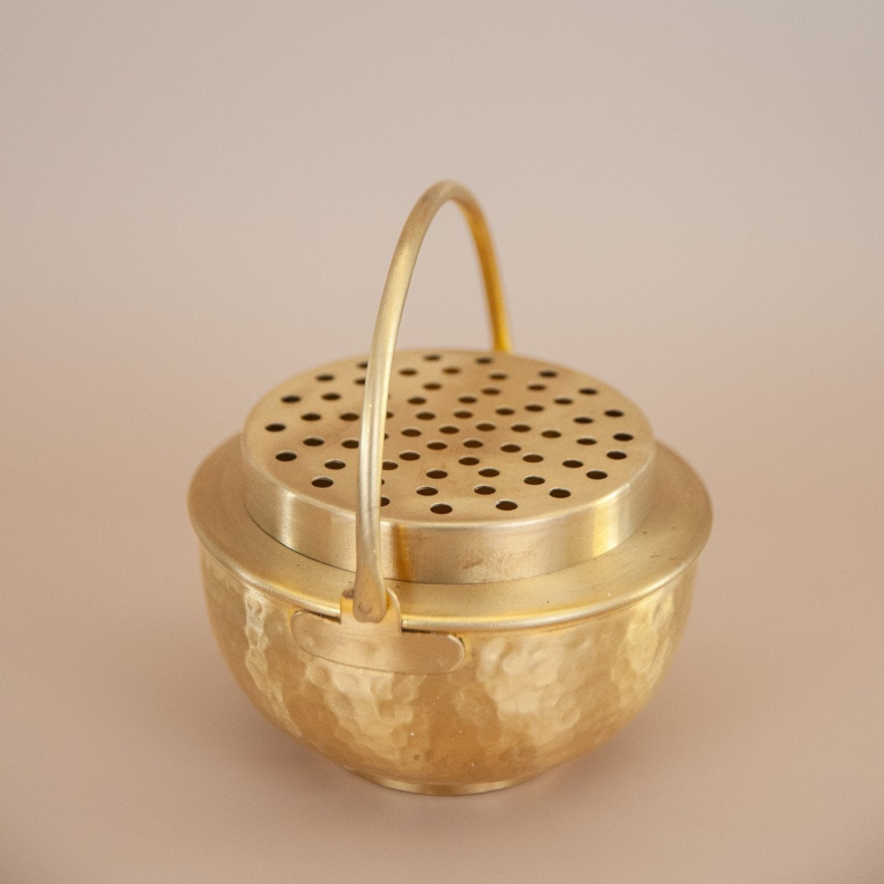 Brass incense burner with a handle on a beige background