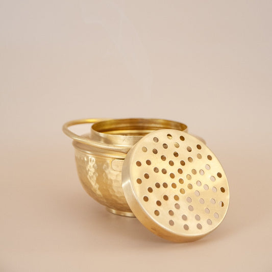 Brass container with perforated lid on a beige background