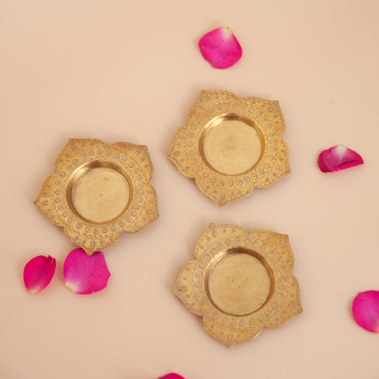 Three gold decorative tealight holders with pink rose petals on a beige background