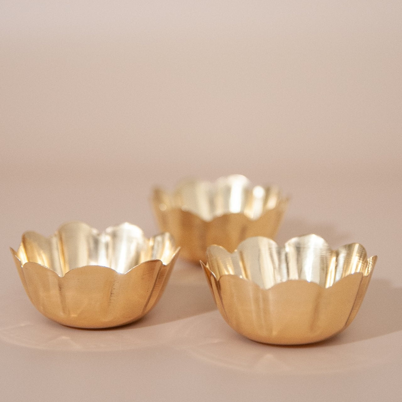 Three brass tealight holders on a beige background