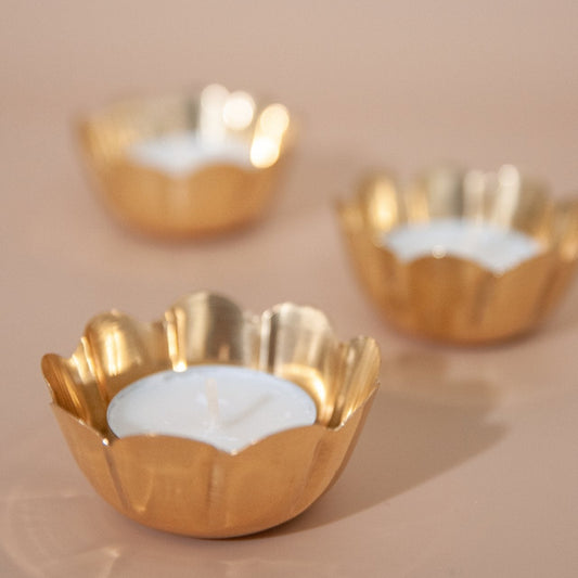 Three brass tealight holders with white candles on a beige background