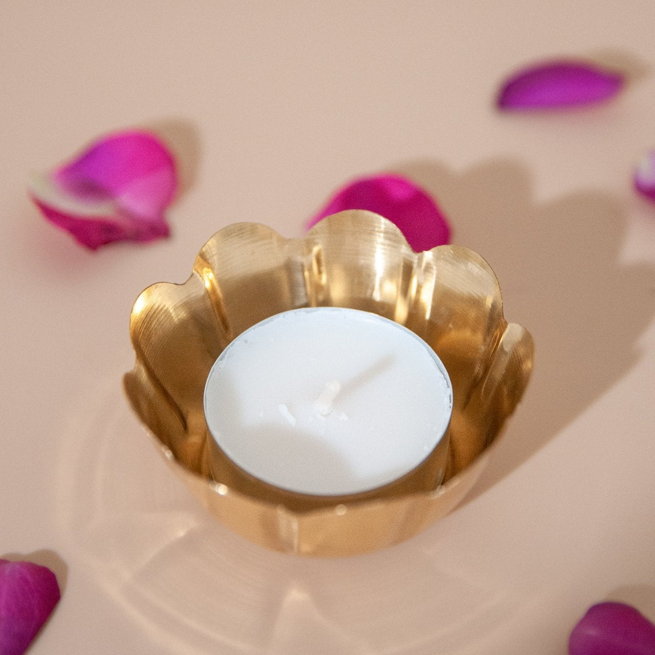 Brass candle holder with a white candle surrounded by pink petals on a beige background