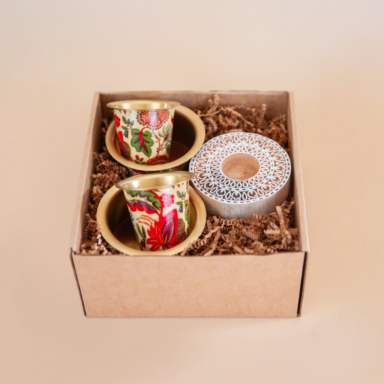 Two enameled brass filter coffee set with a wooden blockprint tealight holder in a gift box on a beige background