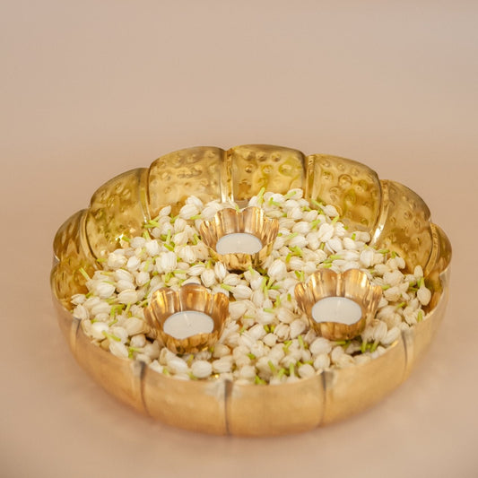 Decorative brass urli bowl with flowers and small  brass candle holders on a beige background