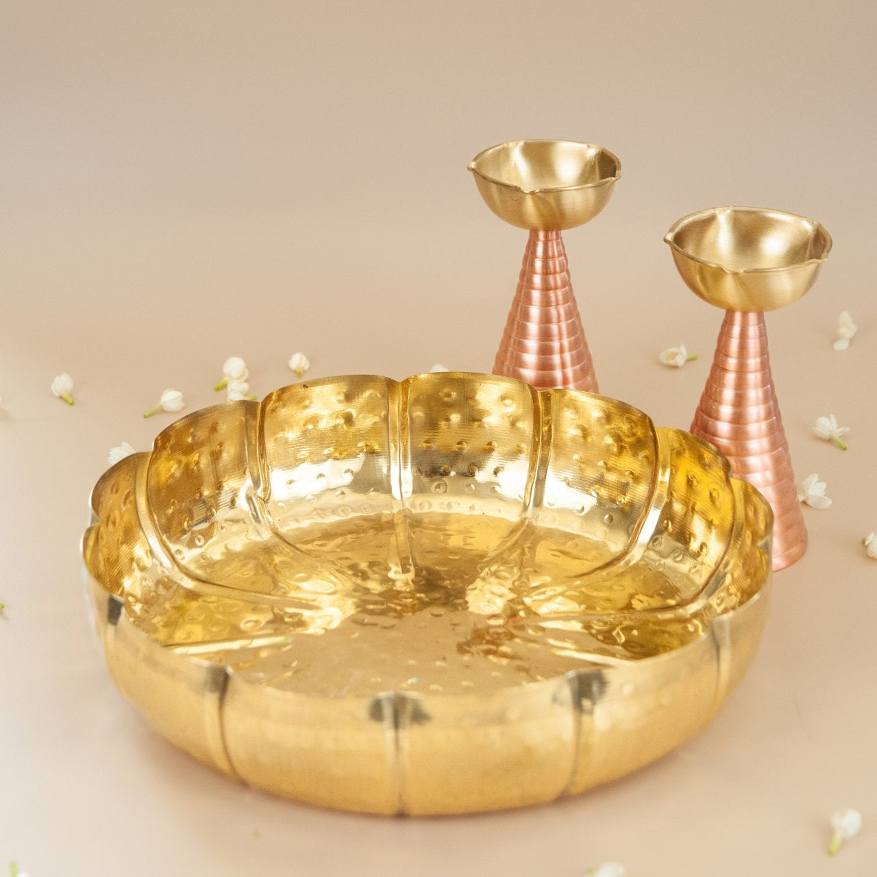 Brass decorative urli bowl with two tall brass diya on a beige background