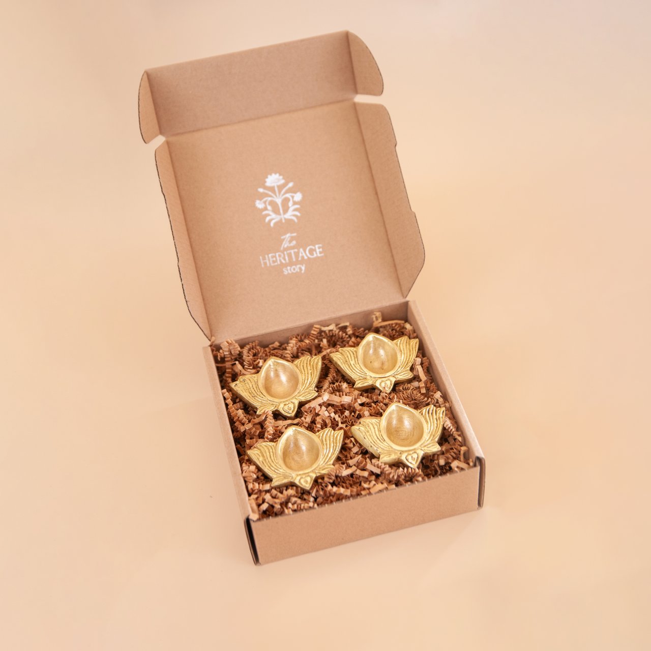 Four brass diyas (oil lamps) in a Heritage story gift box on a beige background