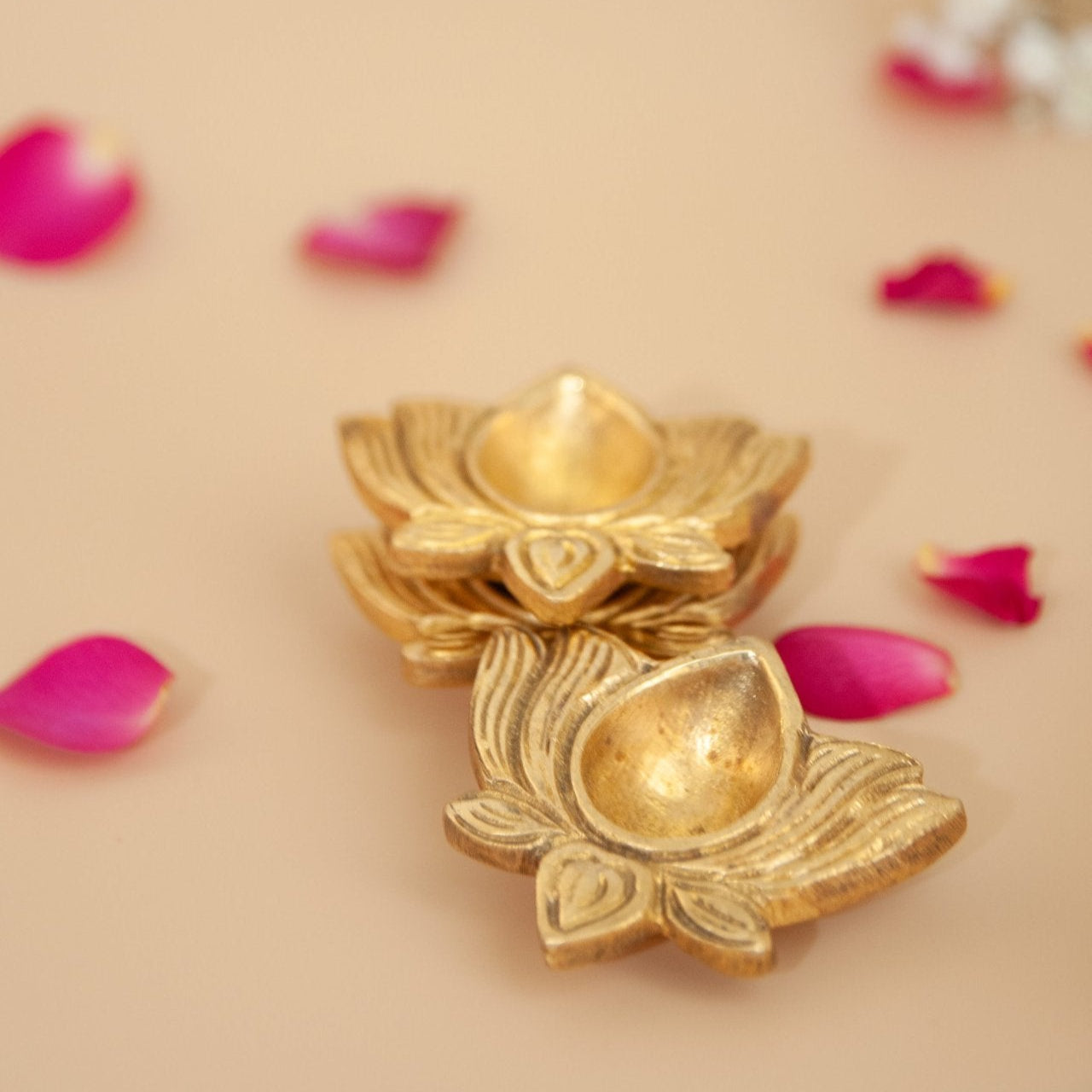 Brass lotus-shaped diya with pink petals on a beige background