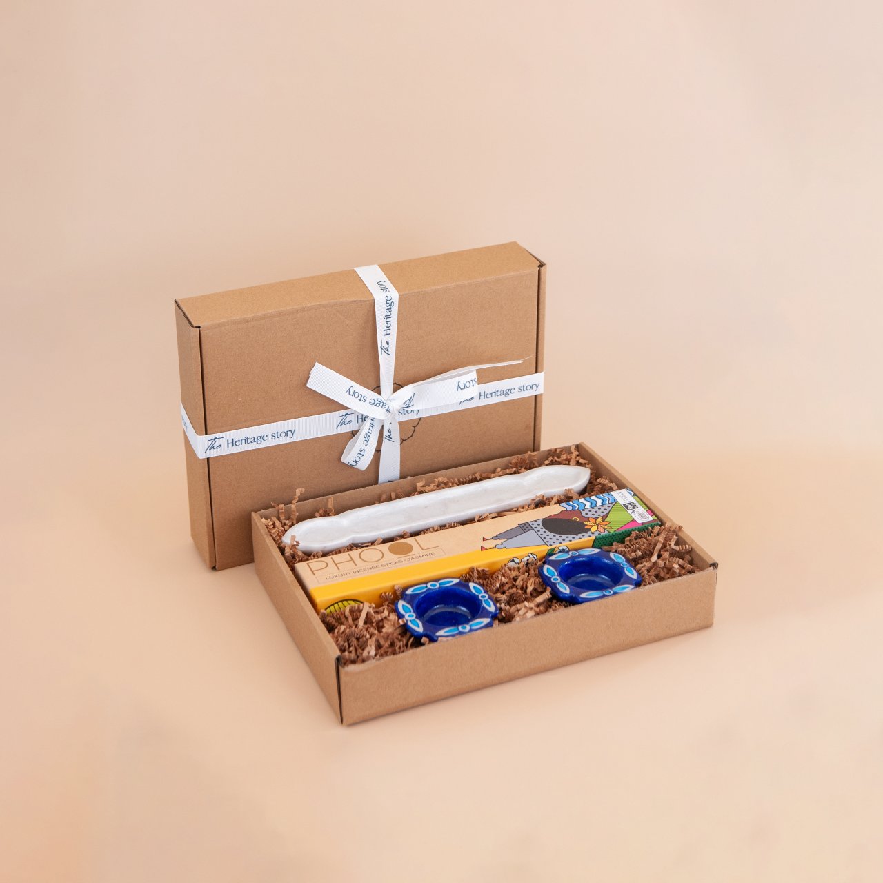 Gift box with a marble incense holder, artisnal incense sticks and blue pottery ealight holders on a beige background