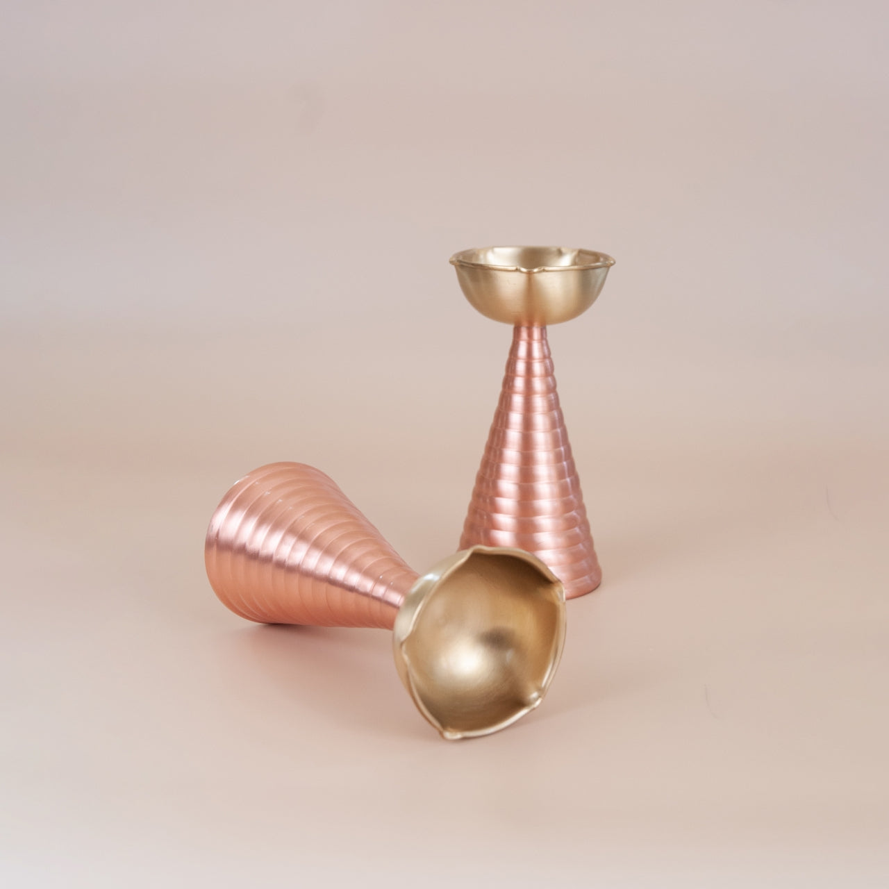Decorative brass candle holders with gold and rose gold finishes on a beige background