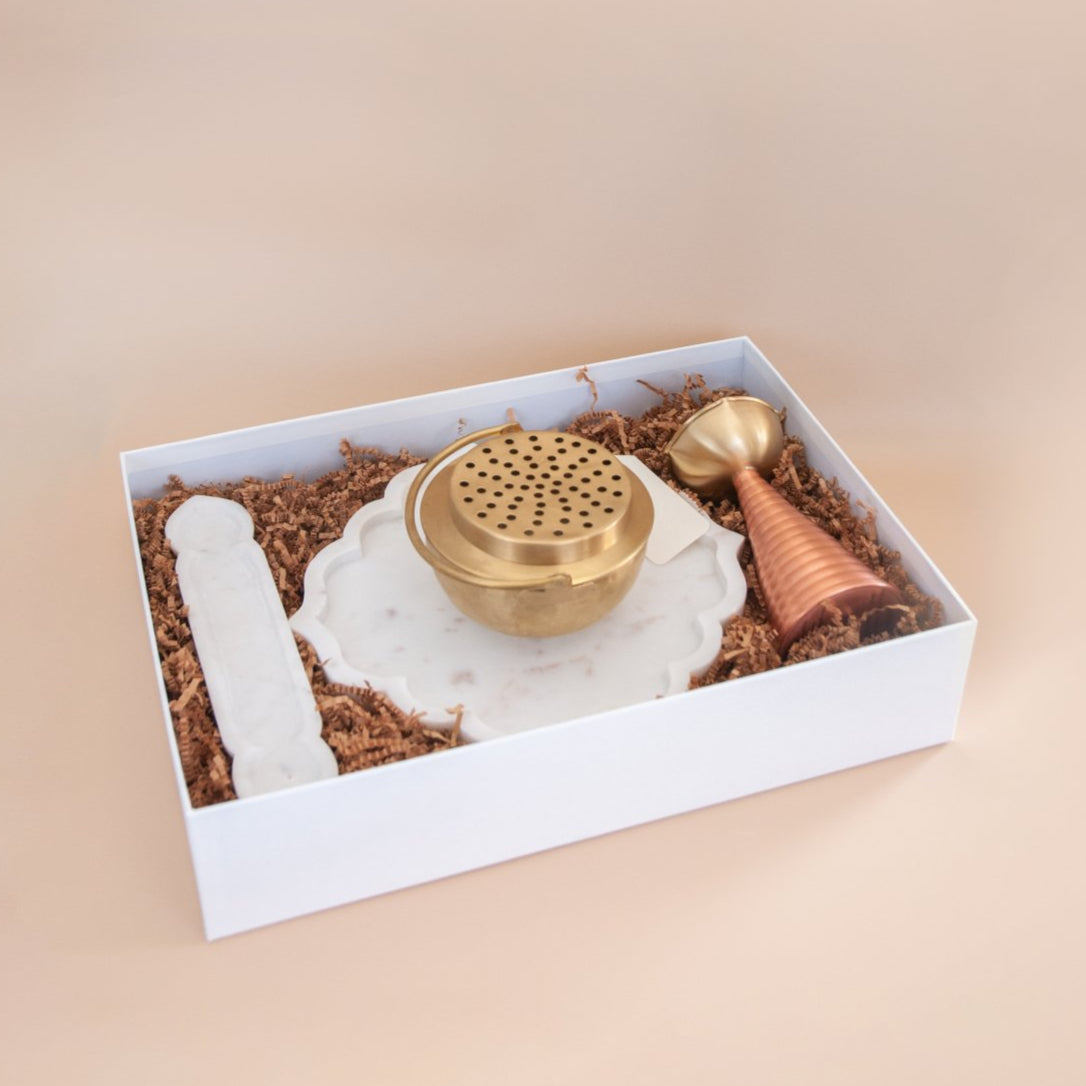 Brass dhuni and 2 tone brass diya with marble platter and marble incense holder in a white gift box set with a beige background