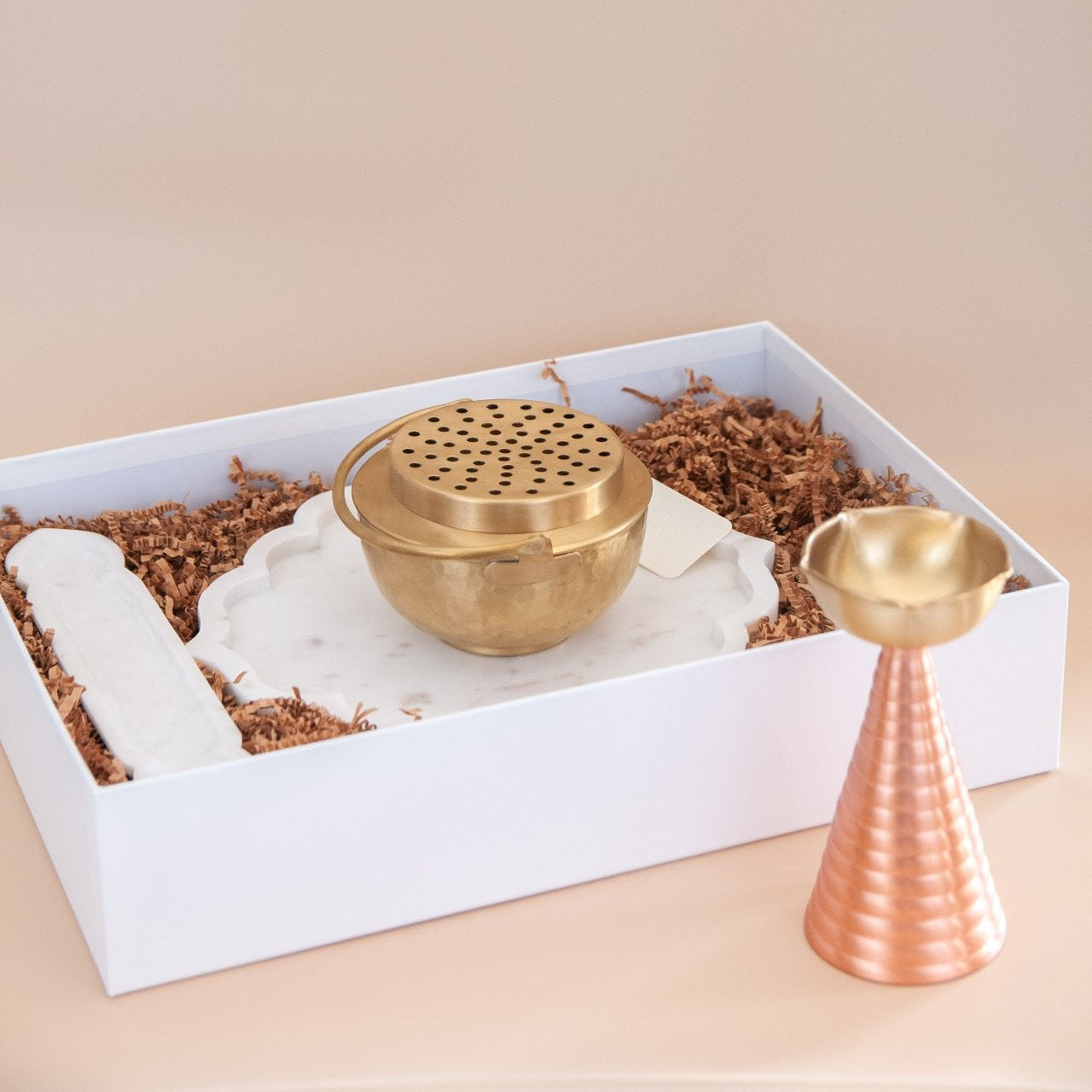 Brass incense burner and holder in a white box with brown tissue on a beige background